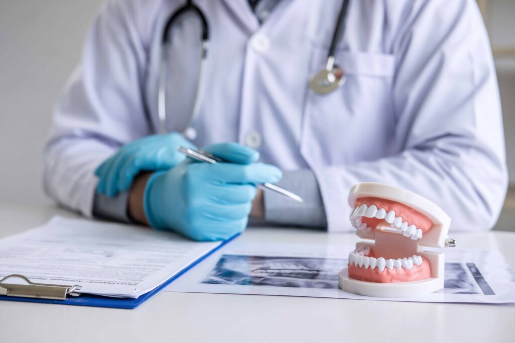 バインダー、レントゲン写真、歯の模型がテーブルに置かれており、その前に座っている歯科医師