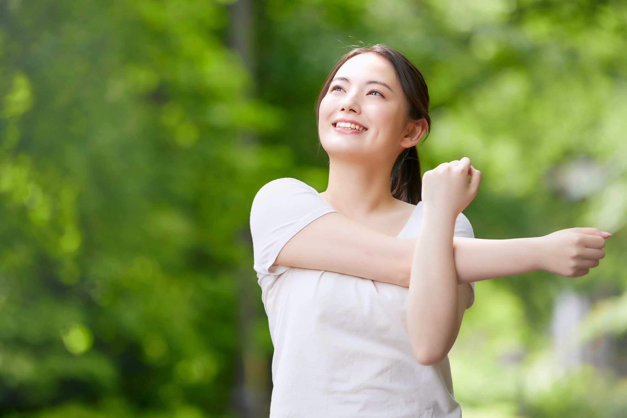 新緑の中でストレッチする笑顔の女性